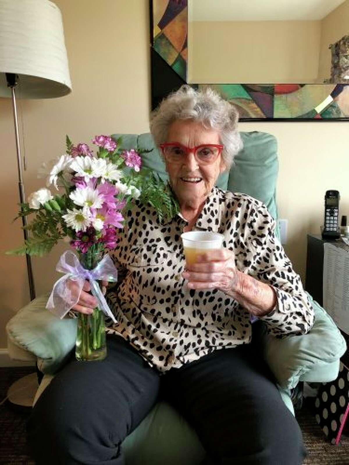 Willa Stauffer, a resident of Primrose Retirement Community, happily enjoys a beverage and a bouquet of fresh-cut flowers in her Midland home. (Photo provided)