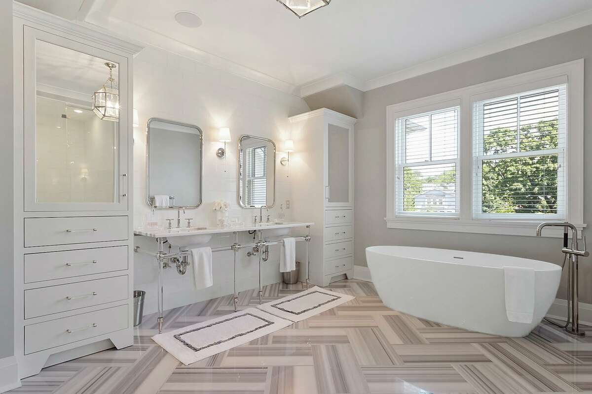 The large and luxurious master bath has large scale marble tile flooring in a herringbone pattern, double vanity, shower, and a soaking tub. On the second floor, the master bedroom suite features a gas log fireplace, sitting area, custom walk-in closets, and a large and luxurious bath with large scale marble tile flooring in a herringbone pattern, double vanity, shower, and a soaking tub. Pocket doors separate the master suite from the separate office or gym. There are three other bedrooms on this level, all of them en suite. The fifth en suite bedroom is on the third floor. It features a built-in bed and ample storage. Outside, there is a built-in grilling area and sliding barn-like doors open to reveal a second wet bar and television viewing area for the patio.