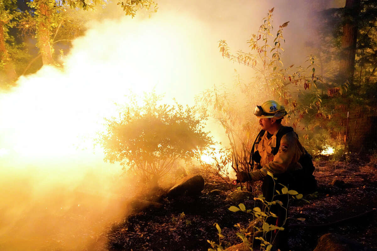 Firefighter Jeremy Damon of the Nevada Yuba Placer Fire Dept. monitors a controlled burn in the backyard of a home in front of the advancing CZU August Lightning Complex Fire Friday, Aug. 21, 2020, in Boulder Creek, Calif. (AP Photo/Marcio Jose Sanchez)