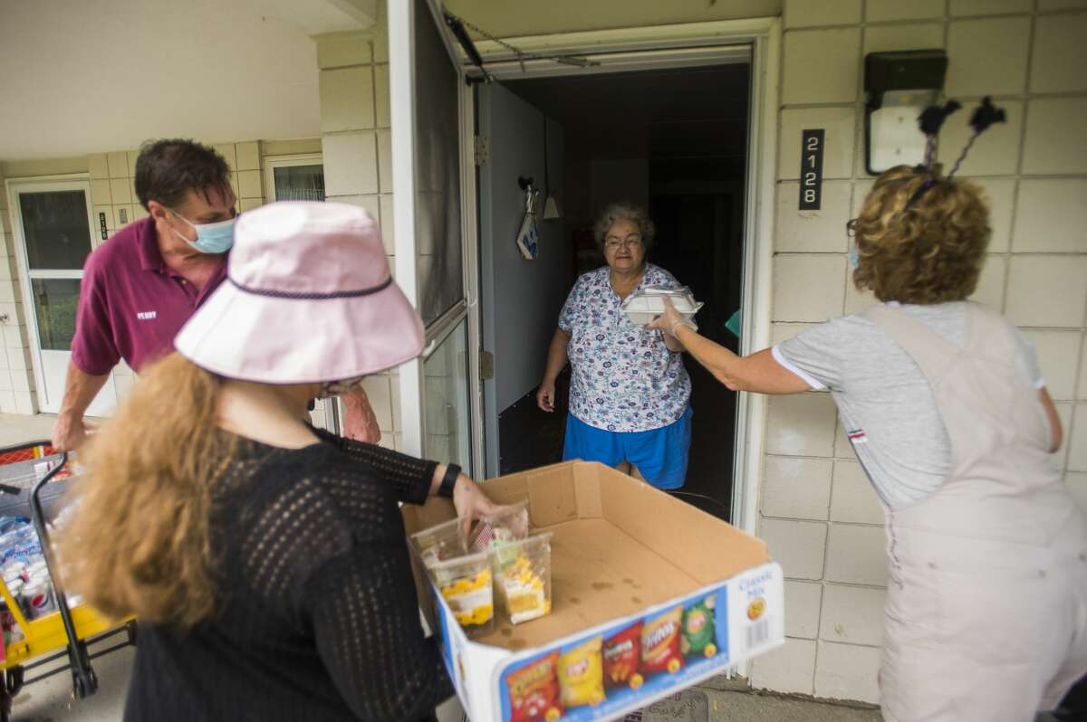 Cleveland Manor Administrative Assistant Marilyn Rease, right, delivers a meal to resident Sandra Johnson, center, during a picnic parade with help from Perry Nunnari, left, and Alexandria Dodge, second from left, Wednesday, Aug. 26, 2020 at the apartment complex in Midland. The facility normally holds a more traditional annual picnic in the courtyard, but made adjustments this year due to COVID-19. (Katy Kildee/kkildee@mdn.net)