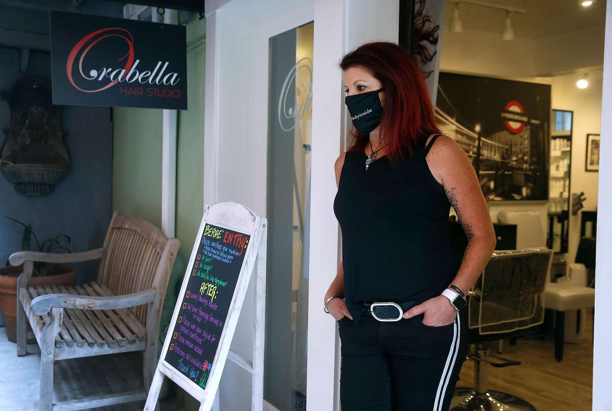 Alicia Orabella stands in the doorway of her hair studio in Oakland, Calif. on Wednesday, Aug. 26, 2020. Orabella has decided against reopening her small studio when Alameda County loosens restrictions on hair salons Friday allowing them to operate outdoors only.