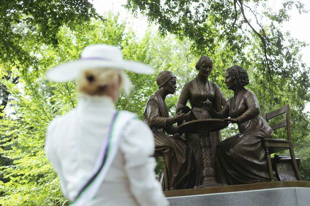 Mona Cahill, costumed as a women suffrage activist, stood in front of the Women’s Rights Pioneers statue in Central Park Wednesday, Aug. 26, 2020, in New York. The statue, created by Ridgefield sculptor Meredith Bergmann and featuring Sojourner Truth, Susan B. Anthony and Elizabeth Cady Stanton, is the first monument in the park honoring any female historical figures.