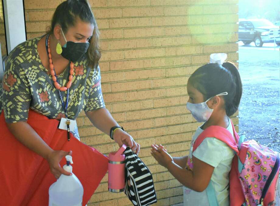 Third-grade teacher Nikki Tibe helps Needville Elementary School student Mia Vazquez clean her hands with sanitizer before entering the building on the first day of school Monday, Aug. 24, 2020. Photo: Courtesy Of Needville ISD