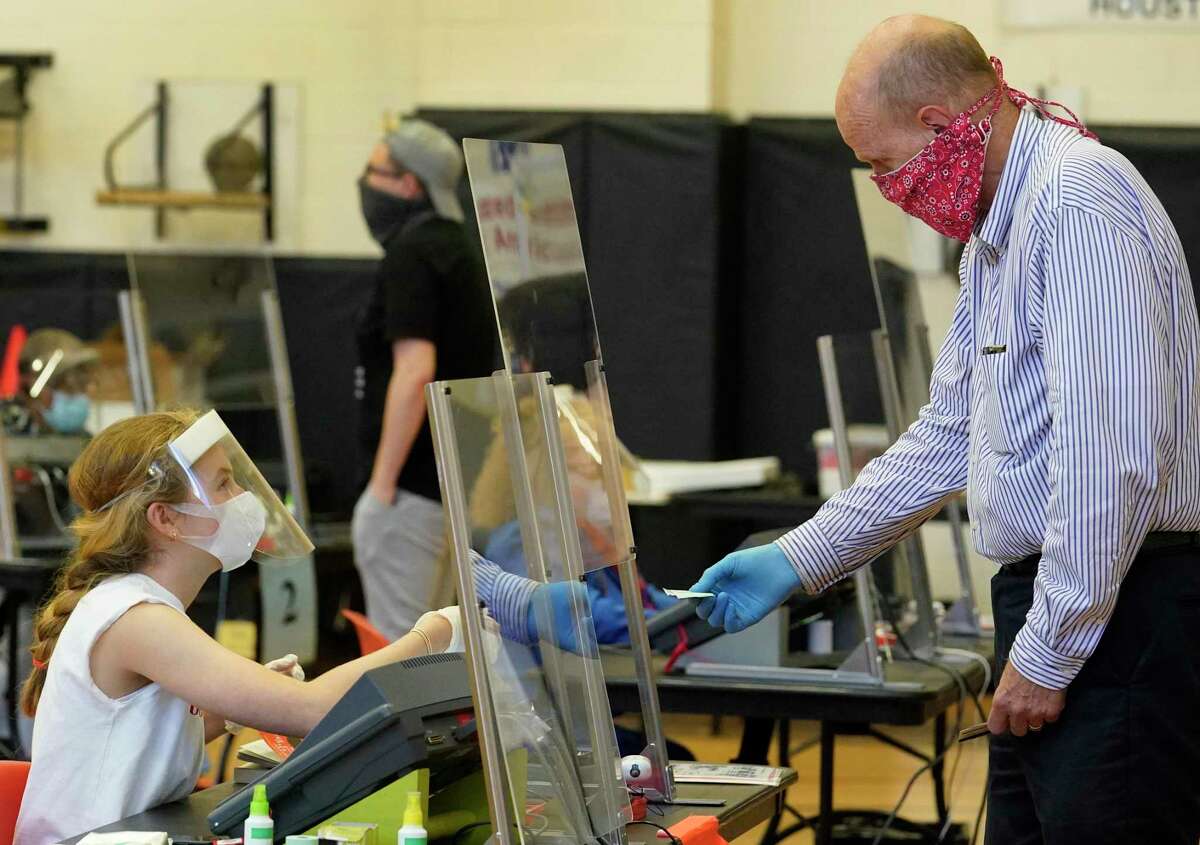 Allison Aungier, an election clerk, left, works behind a plastic barrier at her desk wearing a face mask, face shield and gloves as she checks in voters at the Metropolitan Multi-Service Center, 1475 West Gray, Friday, July 10, 2020, in Houston.