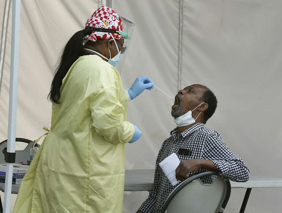 A healthcare worker collects an oral sample from a resident at a walk-up COVID-19 testing site at the Roots Community Health Center in Oakland, Calif. on Wednesday, Aug. 26, 2020.