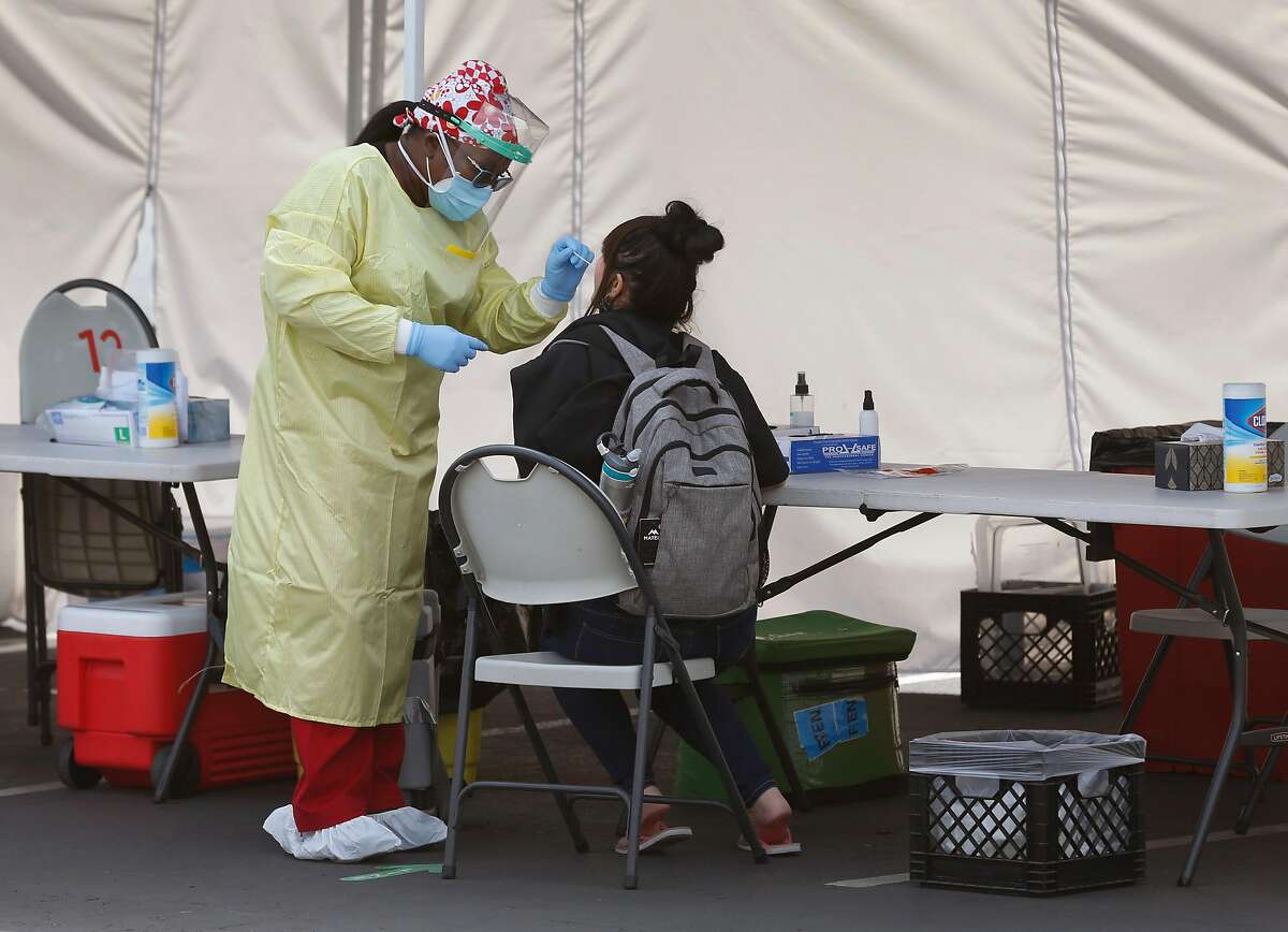 A healthcare worker collects an oral sample from a resident at a walk-up COVID-19 testing site at the Roots Community Health Center in Oakland, Calif. on Wednesday, Aug. 26, 2020. Infection rates of the coronavirus appears to be slowing throughout the Bay Area.