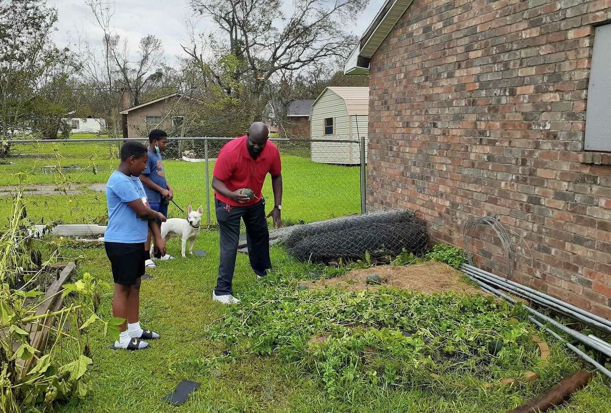 David Miller salvages a tiny watermelon from his flattened garden behind his house in Lake Charles. Sons, William (left) and David III, along with their fog, Bill, survey the damage.