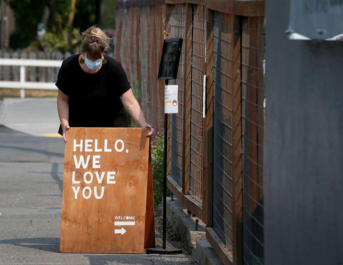 Boon restaurant general manager Mags van der Veen arranges a sign to attract diners after reopening in Guerneville, Calif. on Saturday, Aug. 29, 2020. The town on the Russian River is gradually reopening after evacuation orders were lifted from the LNU Lightning Complex fires.