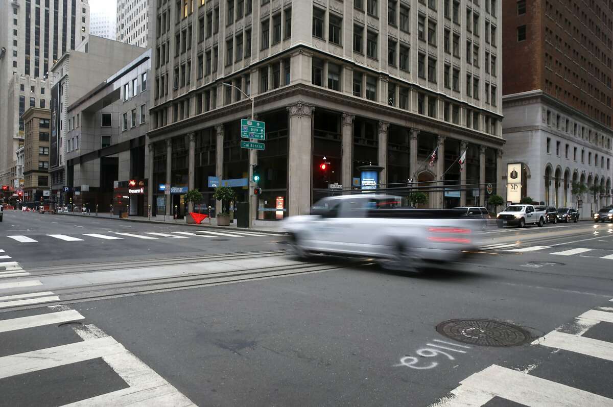 A vehicle rolls through the deserted intersection of California and Battery streets during the morning commute in San Francisco, Calif. on Tuesday, Aug. 25, 2020. Some businesses have remained open despite few office workers and commuters populating the Financial District during the coronavirus shutdown.