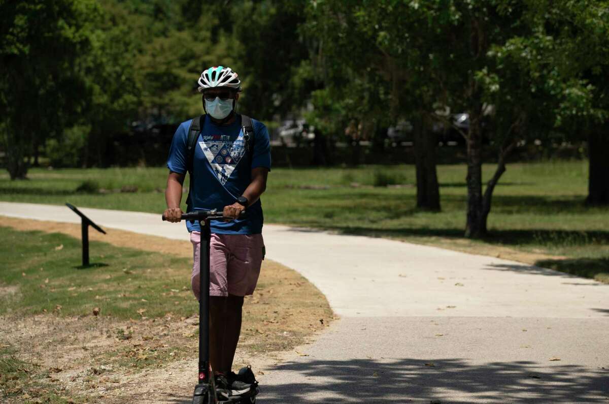 A man rides an electronic scooter with a mask on along the Brays Bayou Greenway Trail on June 18, 2020, at Hermann Park in Houston.