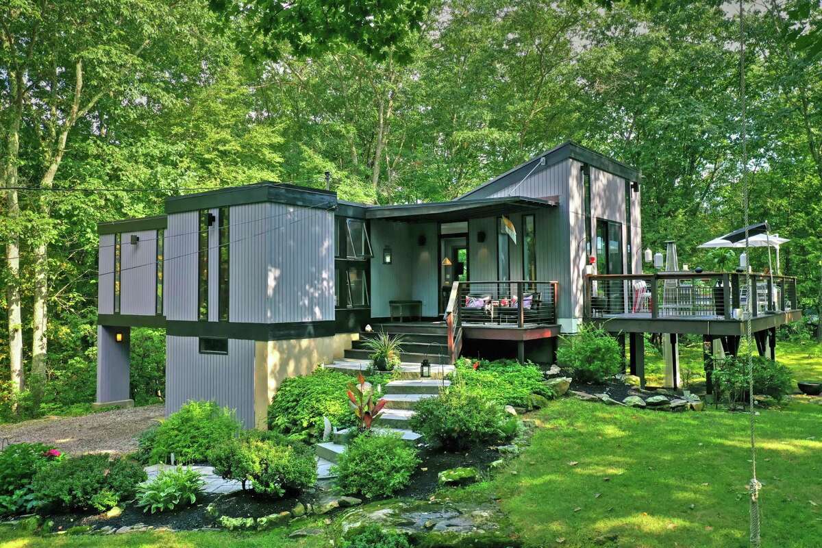 The gray custom-built contemporary house at 75 Birch Hill Road sits on a property of just over two acres near the center of Weston. This house was built in 1968, about three years after the end of midcentury modern period, yet it dovetails perfectly into the 21st century way of life. And just as iconic architect Frank Lloyd Wright set his mid-century modern masterpieces near water features, this property also contains a pond. The "sleek, sophisticated, light and bright" house is set back from the road in the heart of Weston on a level and lightly wooded property of just over two acres looking as much like a contemporary sculpture as like a residence. Honoring its private setting located on a cul-de-sac, this house invites indoor-outdoor living. It features a large wrap-around raised deck with a stainless steel cable railing and curved stairway to lower patio - perfect places for al fresco dining, relaxing, or simply enjoying the view, and a second smaller deck/covered front porch.
