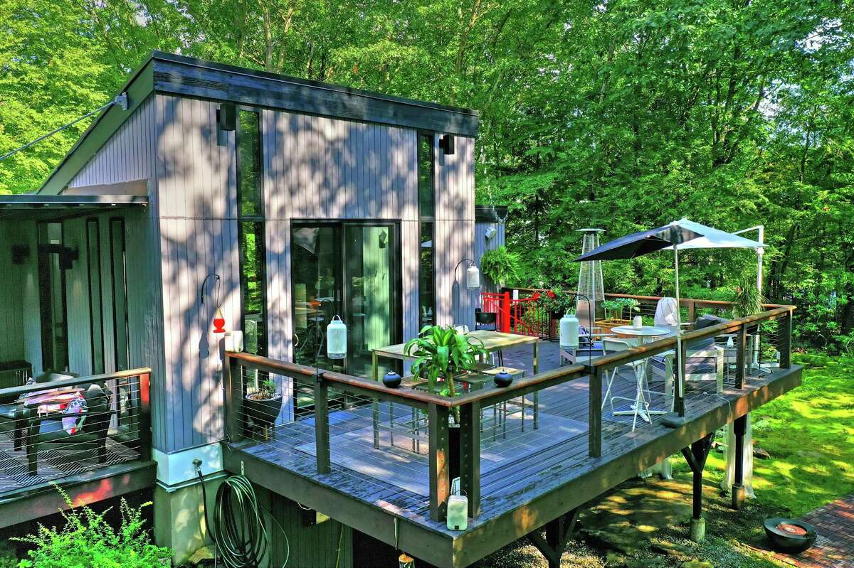 Indoor-outdoor living is encouraged by the numerous sets of sliding doors to the large wrap-around deck and the patio below. The master bedroom offers a walk-in closet and a private balcony. The second main level bedroom also has a private balcony, and it is just steps away from the hall bath, which features a deep soaking tub. One of the home's three full baths, the master bath, is more sophisticated and luxurious with a large scale tile backsplash in the glass shower, a contemporary vanity, and radiant heated floor. The other on the main level is much more rustic, paying homage to the wooded setting, featuring pinewood paneling, although the soaking tub befits the contemporary style of the house.