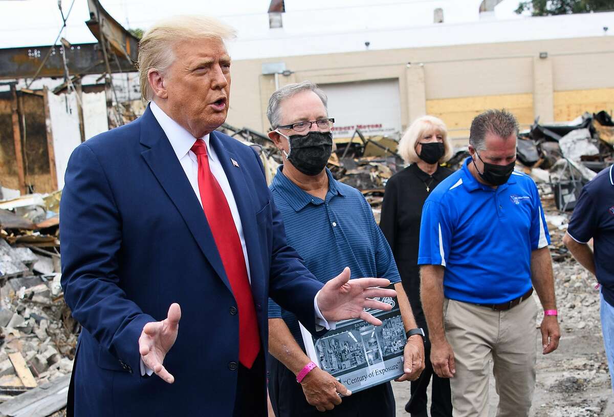 US President Donald Trump speaks to the press as he tours an area affected by civil unrest in Kenosha, Wisconsin on September 1, 2020, as John Rode(C), the former owner of Rode's Camera Shop looks on holding a sign. - Trump said Tuesday on a visit to protest-hit Kenosha, Wisconsin that recent anti-police demonstrations in the city were acts of "domestic terror" committed by violent mobs. "These are not acts of peaceful protest but really domestic terror," Trump said, describing multiple nights of angry demonstrations last week after a white police officer in Kenosha shot a black man in the back at close range. (Photo by MANDEL NGAN / AFP) (Photo by MANDEL NGAN/AFP via Getty Images)