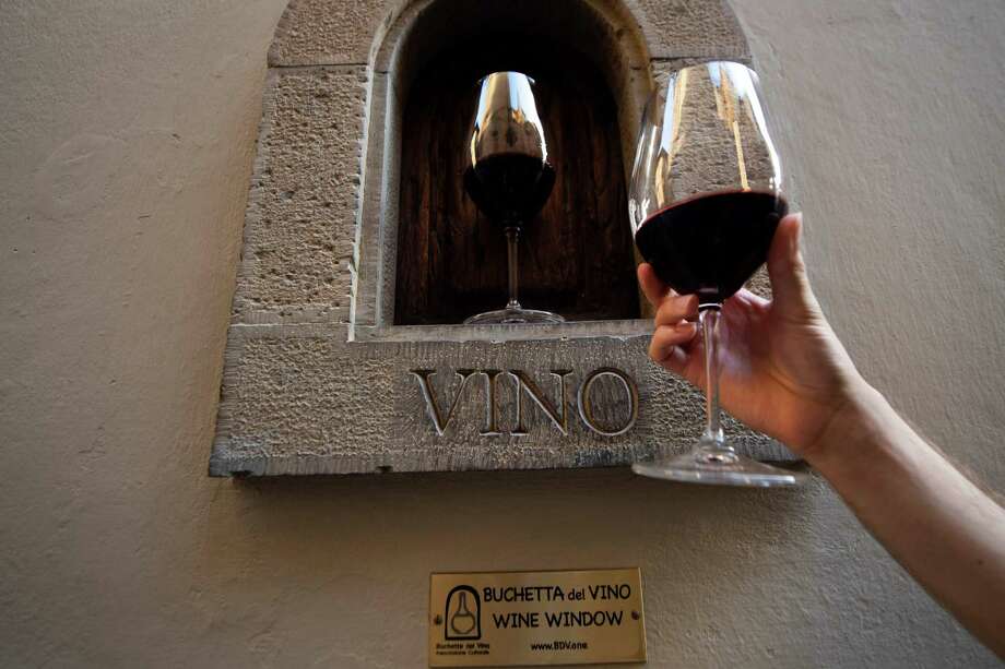 A person holds a glass of wine next to the "buchetta del vino" a small window to serve wine a tradition which exists since the Renaissance and that is typical in the streets of Florence, on August 12, 2020. - As 16th-century Florentines dropped like flies to the plague, survivors drowned their fears in wine, passed to them through small windows which are enjoying a renaissance during the coronavirus era. The small "wine windows" can be seen dotted around the Tuscan capital next to the grand entrances of sumptuous noble palaces, where wealthy families used to sell alcohol directly to thirsty customers, passing flasks through to eager hands. (Photo by Tiziana FABI / AFP) (Photo by TIZIANA FABI/AFP via Getty Images) Photo: TIZIANA FABI / AFP Via Getty Images / AFP or licensors