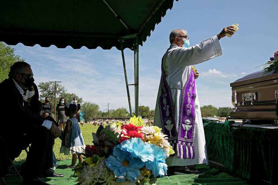 Enrique, left, watches as Deacon Adrian Falcon, from Our Lady of Guadalupe Church, blesses Nora, his wife of almost 44 years, during her burial service at at Sunset Memorial Oaks Cemetery in Del Rio. Nora was hospitalized June 19 with COVID-19. Coronavirus restrictions prevented Enrique and the rest of the family from being at her bedside during her illness. Photo: Lisa Krantz, Staff Photographer / San Antonio Express-News