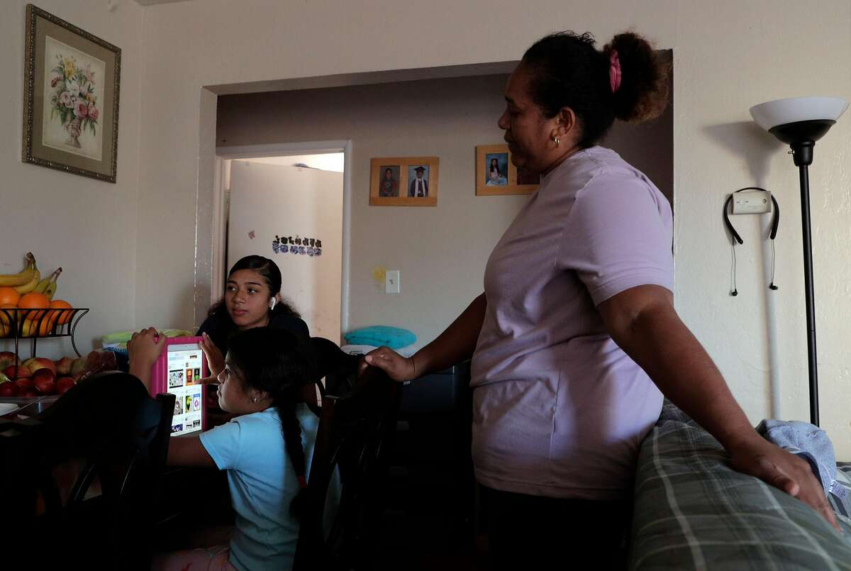 Elena Sabay, right, looks over her daughter Dayana's shoulder as she plays on her ipad, with Johmara, 14, rear as the Romero family spends time at home in Oakland, Calif., on Monday, July 13, 2020. Elena Sabay recently lost her job as hotel housekeeper because of business shutdowns and her husband’s, Alfredo Romero, earnings are the only thing keeping the family afloat during the pandemic.