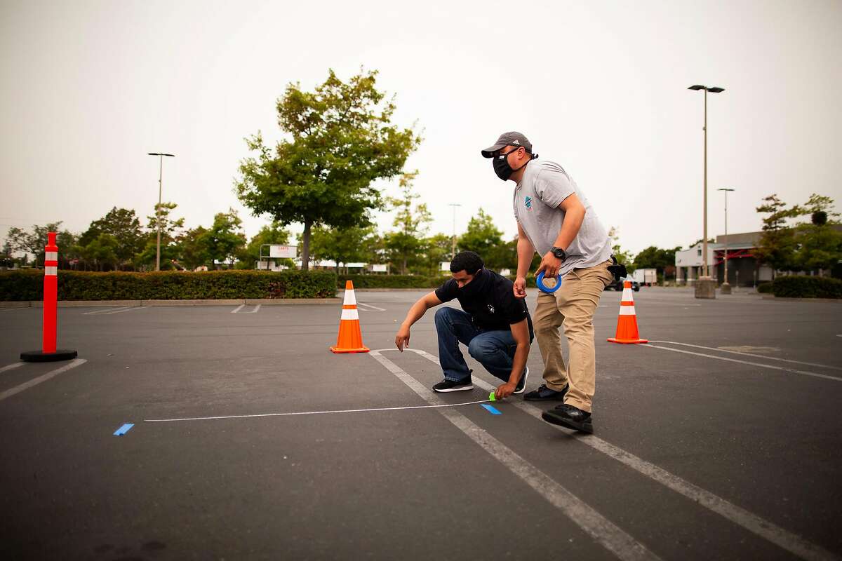 Guillermo Sabas (left) and Jeovanny Torrez measure and lay down tape to mark 6 feet for social distancing at a PG&E community resource center in the parking lot of Costco, Santa Rosa, California, September 8th, 2020. The center is providing water, snacks, charging stations, shade and other items to people who lost power to PG&E power cuts to prevent wildfires.