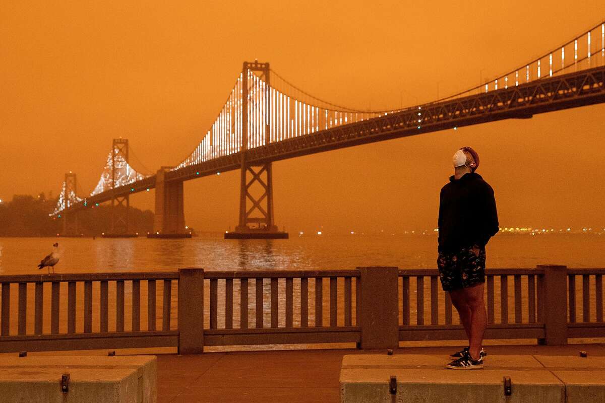 Eli Harik of San Francisco wears a mask while looking up at the dark orange sky hanging over the Embarcadero in downtown San Francisco, Calif. Wednesday, September 9, 2020 due to multiple wildfires burning across California and Oregon.