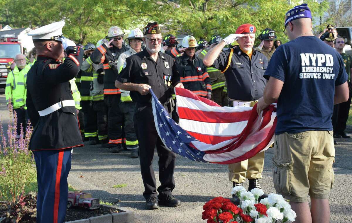 Spectrum/The town of New Milford recognized the 18th anniversary of 9/11 with a morning ceremony held at the town's 9/11 memorial in Patriot's Way. The event, coordinated by the town's 9/11 Committee, included a prayer, the tolling of Water Witch Hose Co. #2's apparatus bell at 8:46 a.m., the presentation of the flag by first responders, remarks by Mayor Pete Bass, State Representatives Bill Buckbee (R-67th) and Richard Smith (R-108th) and State Senator Craig Miner (R-30th), and music by St. Francis Xavier Church Choir and Patrick Maguire on bagpipes. In addition to police, fire and ambulance members, the New Milford Police Guard and members of CERT were present. At the conclusion of the ceremony, first responders placed flowers at the base of the memorial. Above, veteran Warren Hengel, left, pauses to receive the flag after, from left to right, Jim Delancy, commander of the VFW in town, Bill Wagner of the VFW Color Guard and veteran Matthew Hayes prepare the flag.