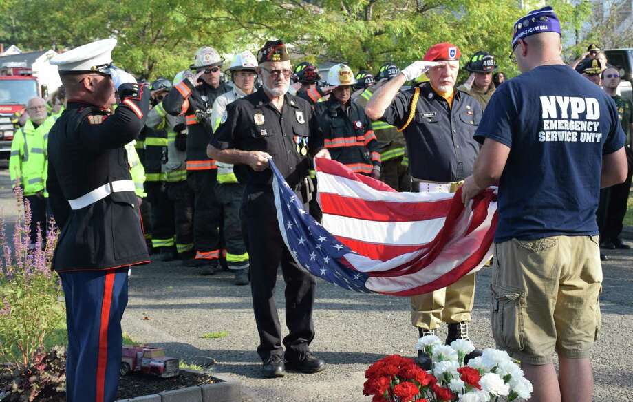 Spectrum/The town of New Milford recognized the 18th anniversary of 9/11 with a morning ceremony held at the town's 9/11 memorial in Patriot's Way. The event, coordinated by the town's 9/11 Committee, included a prayer, the tolling of Water Witch Hose Co. #2's apparatus bell at 8:46 a.m., the presentation of the flag by first responders, remarks by Mayor Pete Bass, State Representatives Bill Buckbee (R-67th) and Richard Smith (R-108th) and State Senator Craig Miner (R-30th), and music by St. Francis Xavier Church Choir and Patrick Maguire on bagpipes. In addition to police, fire and ambulance members, the New Milford Police Guard and members of CERT were present. At the conclusion of the ceremony, first responders placed flowers at the base of the memorial. Above, veteran Warren Hengel, left, pauses to receive the flag after, from left to right, Jim Delancy, commander of the VFW in town, Bill Wagner of the VFW Color Guard and veteran Matthew Hayes prepare the flag. Photo: Deborah Rose / Hearst Connecticut Media / The News-Times / Spectrum