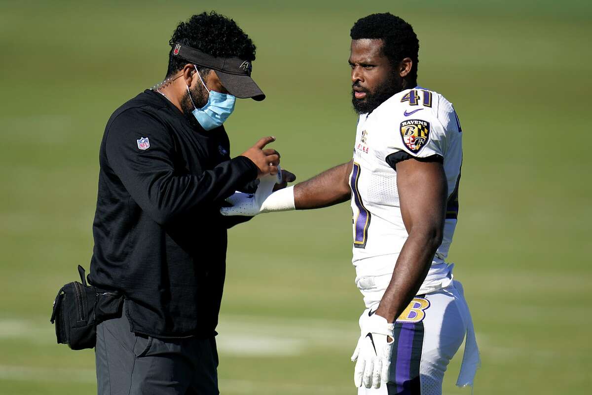 A Baltimore Ravens staff member wears a face mask to protect against COVID-19 while putting tape on the wrist of safety Anthony Levine Sr. during an NFL football camp practice, Tuesday, Aug. 18, 2020, in Owings Mills, Md. (AP Photo/Julio Cortez)