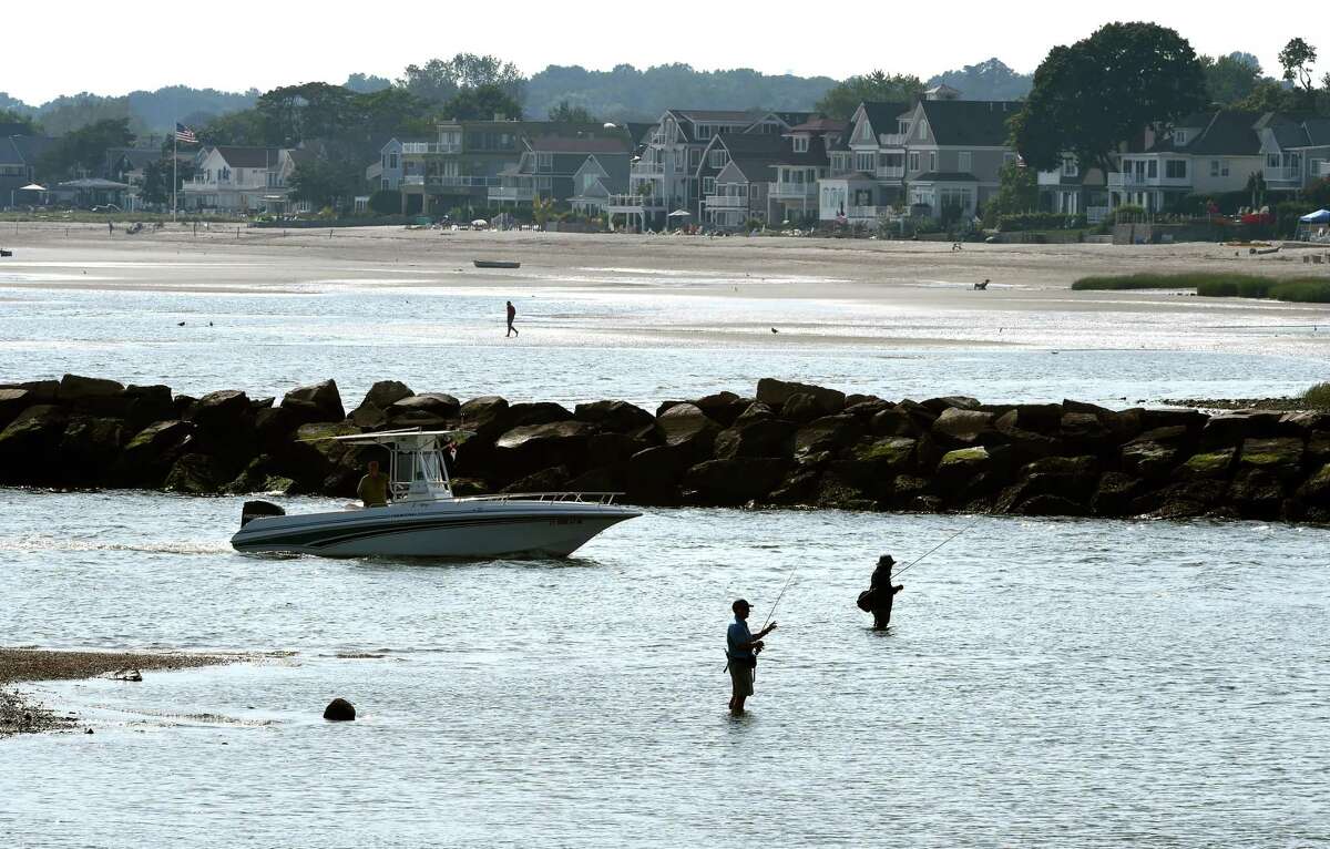 People fish at the mouth of Milford Harbor near Gulf Beach as a boat enters from Long Island Sound on September 11, 2019.