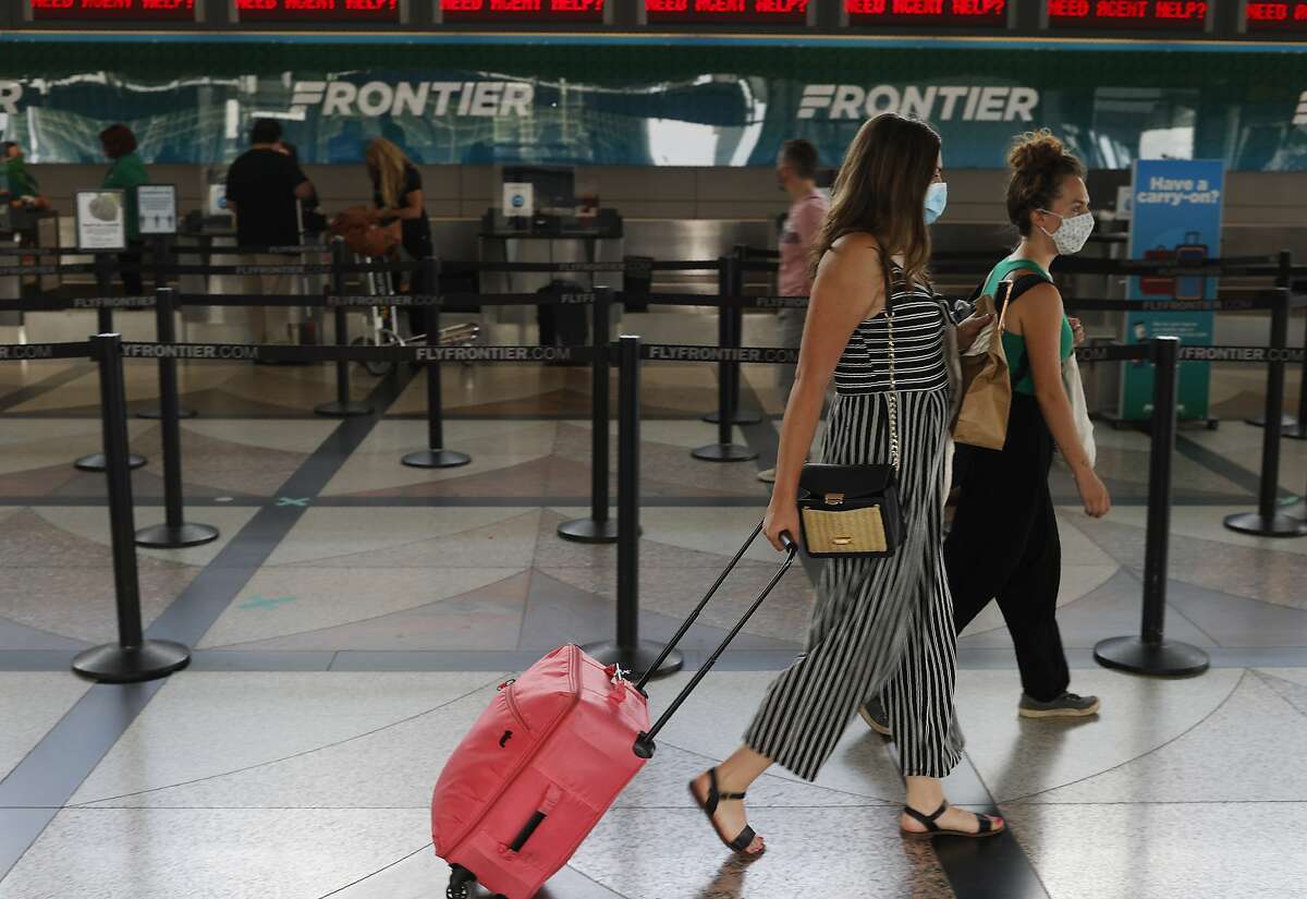 A pair of masked travelers head to the ticketing counter for Frontier Airlines in the main terminal of Denver International Airport Wednesday, July 22, 2020, in Denver. (AP Photo/David Zalubowski)