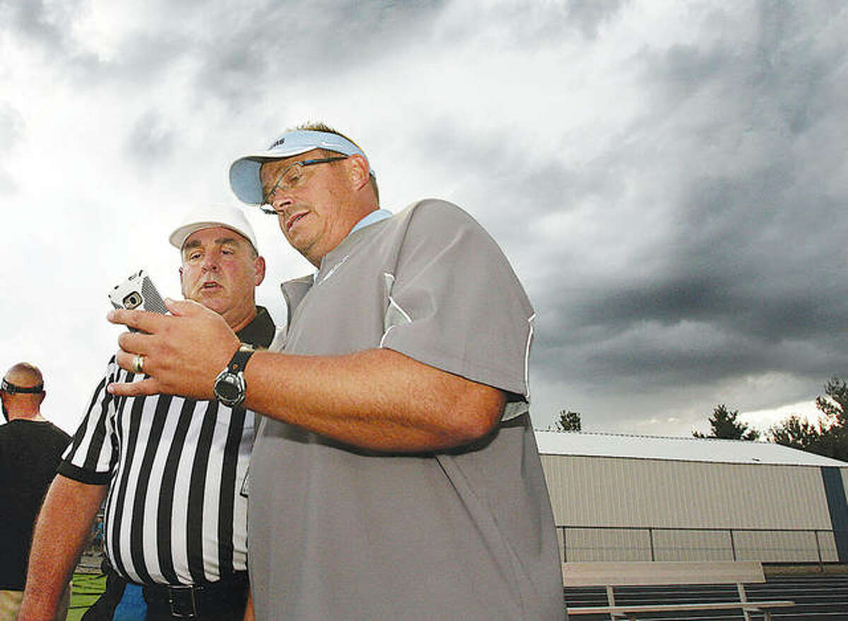 With storm clouds forming behind them, Jersey coach Dave Jacobs and referee Curtis May look at a weather map on Jacobs’ phone during a 2014 game that was postponed on a Friday night and played the next day. With prep football enduring a different kind of storm in 2020, a #Let Us Play Rally will be held at 1 p.m. Saturday at the State Capitol in Springfield.