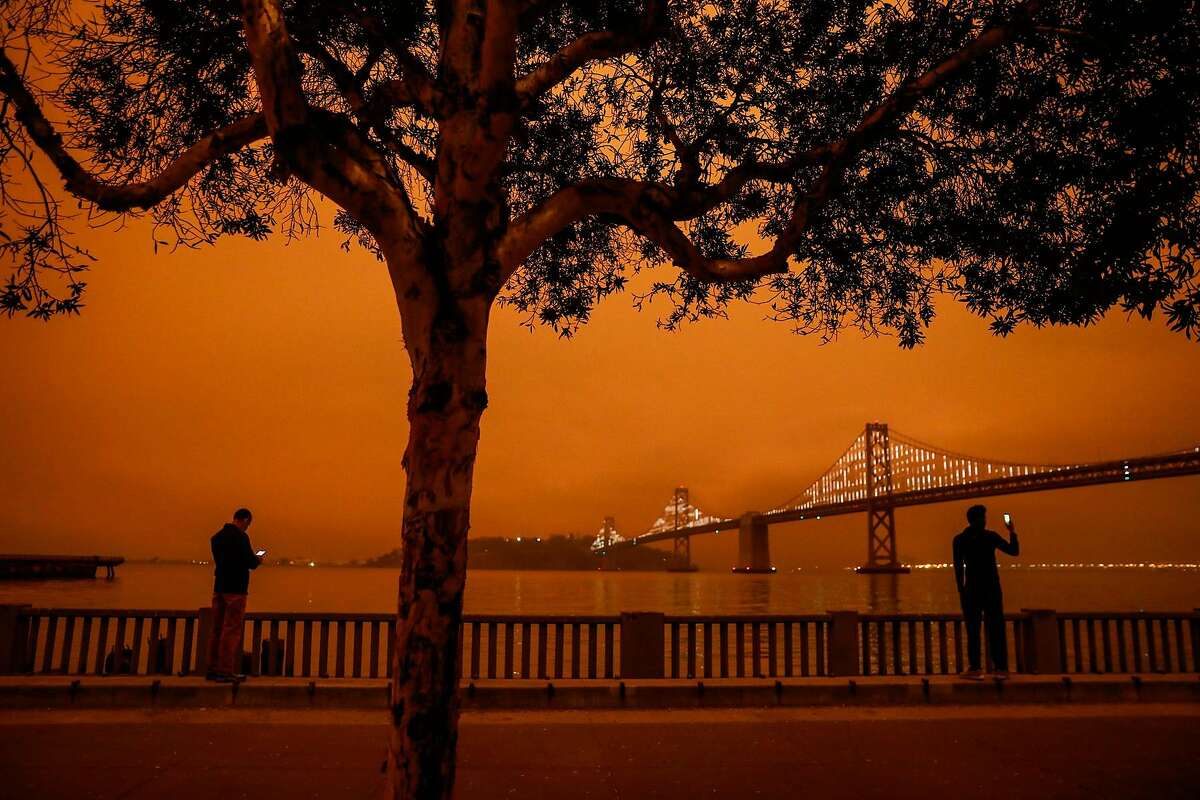 Juan Marmol (left) and another man take footage of the sky next to the Bay Bridge as dark orange skies hang over downtown San Francisco, Calif. Wednesday, September 9, 2020 due to multiple wildfires burning across California and Oregon.