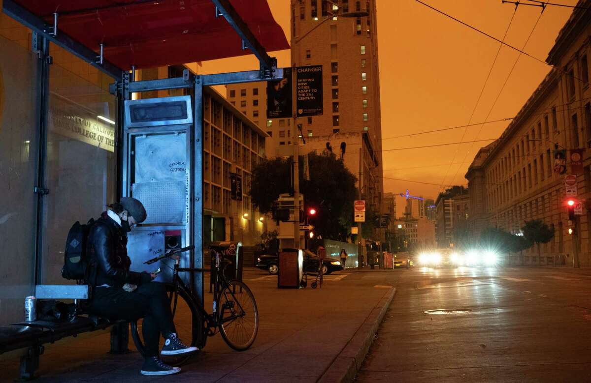 A person waits at a bus stop around noon Sept. 9 in San Francisco.