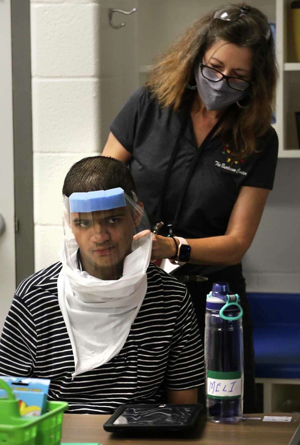 Lavonne Hill, above, an assistant teacher at the Burleson School for Innovation and Education in Edgewood ISD, helps Melchor Ibarra with his mask and face shield Thursday.