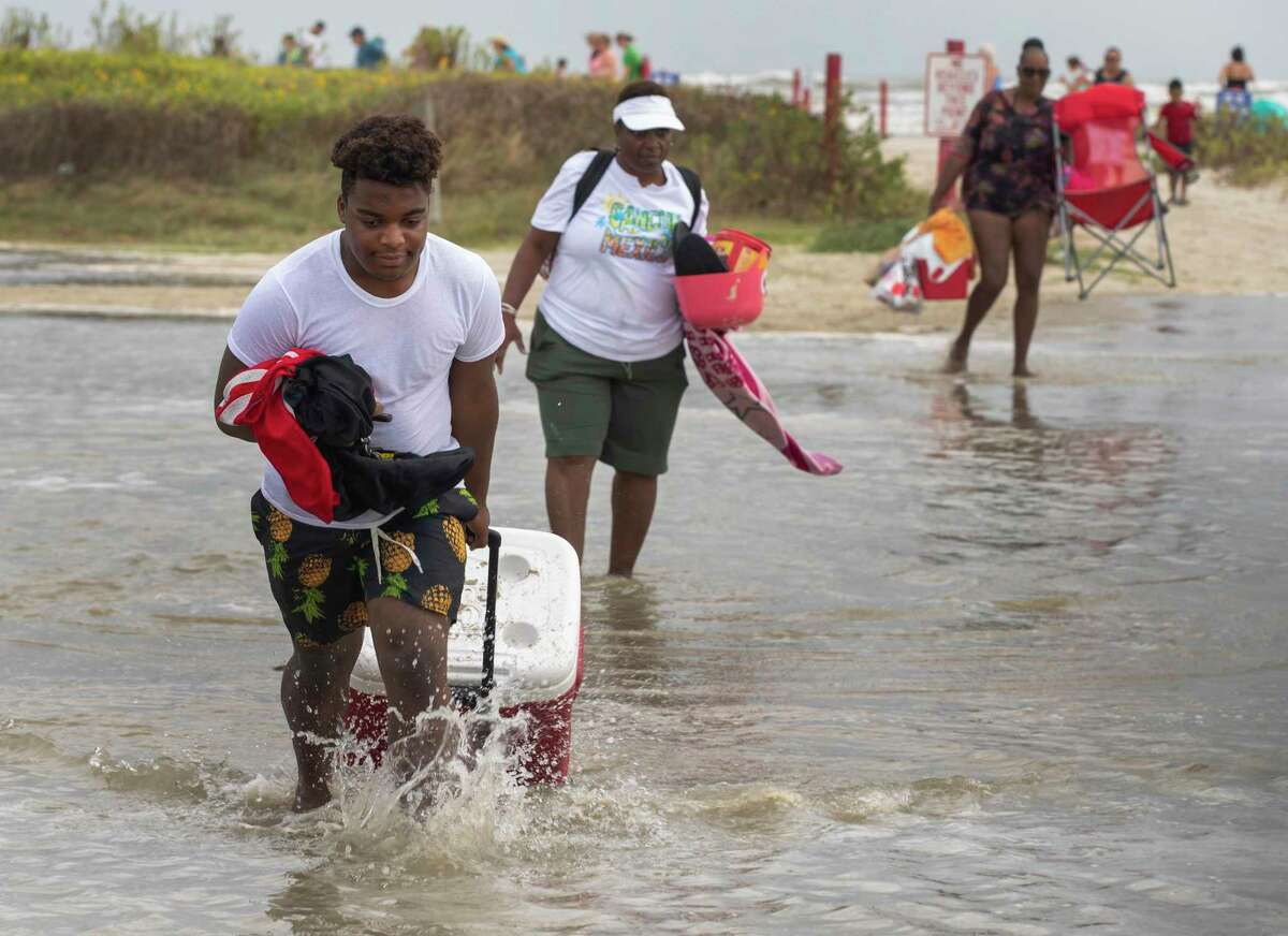 Tyler Heads totes his belongings through tidewaters as he and other beachgoers cross the flooding Stewart Beach parking lot in Galveston, Texas on Saturday, Sept. 19, 2020. Tropical Storm Beta continues to move through the Gulf of Mexico and is expected to bring tidal surge and heavy rain to the area. (Stuart Villanueva/The Galveston County Daily News via AP)
