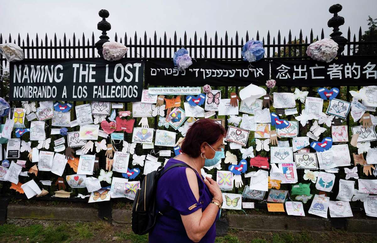 FILE - In this May 28, 2020, file photo, a woman passes a fence outside Brooklyn's Green-Wood Cemetery adorned with tributes to victims of COVID-19 in New York. The U.S. death toll from the coronavirus topped 200,000 Tuesday, Sept. 22, a figure unimaginable eight months ago when the scourge first reached the worldas richest nation with its sparkling laboratories, top-flight scientists and towering stockpiles of medicines and emergency supplies. (AP Photo/Mark Lennihan, File)
