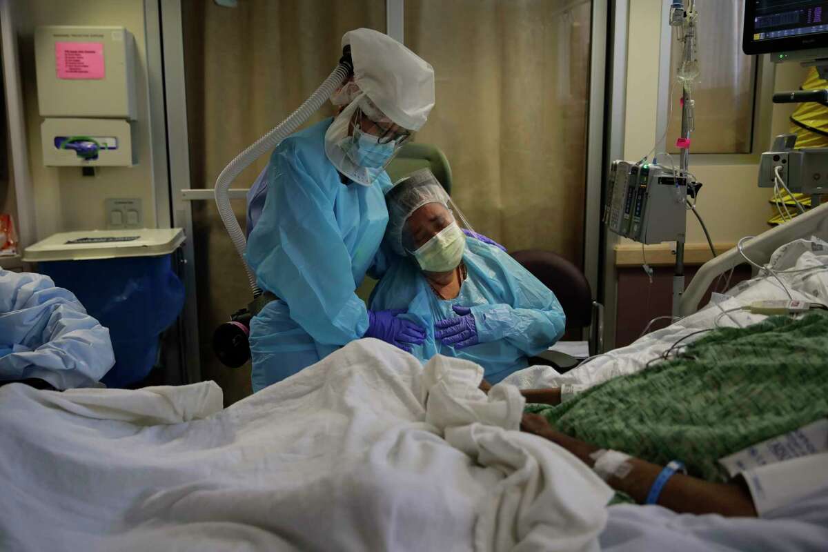 FILE - In this July 31, 2020, file photo, Romelia Navarro, right, is comforted by nurse Michele Younkin as she weeps while sitting at the bedside of her dying husband, Antonio, in St. Jude Medical Center's COVID-19 unit in Fullerton, Calif. The U.S. death toll from the coronavirus topped 200,000 Tuesday, Sept. 22, a figure unimaginable eight months ago when the scourge first reached the worldas richest nation with its sparkling laboratories, top-flight scientists and towering stockpiles of medicines and emergency supplies. (AP Photo/Jae C. Hong, File)