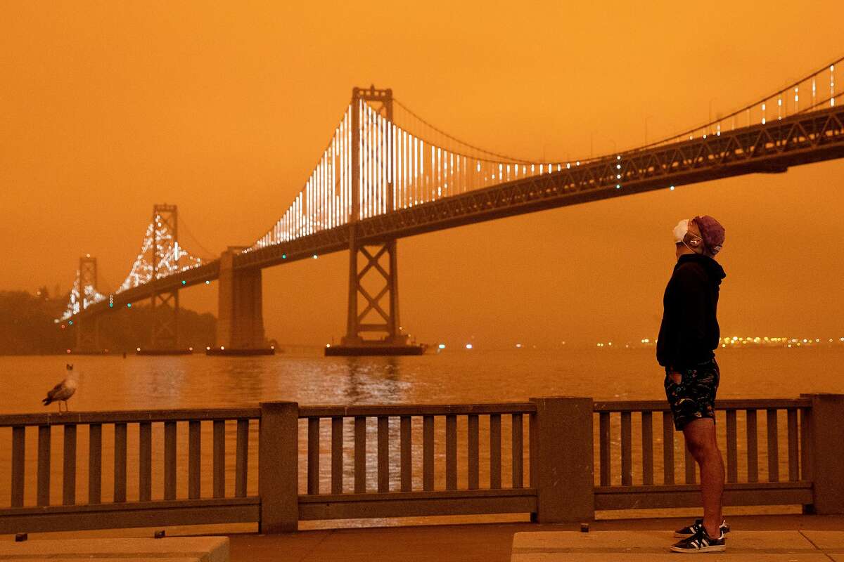 Eli Harik of San Francisco wears a mask while looking up at the dark orange sky hanging over the Embarcadero in downtown San Francisco, Calif. Wednesday, September 9, 2020 due to multiple wildfires burning across California and Oregon.