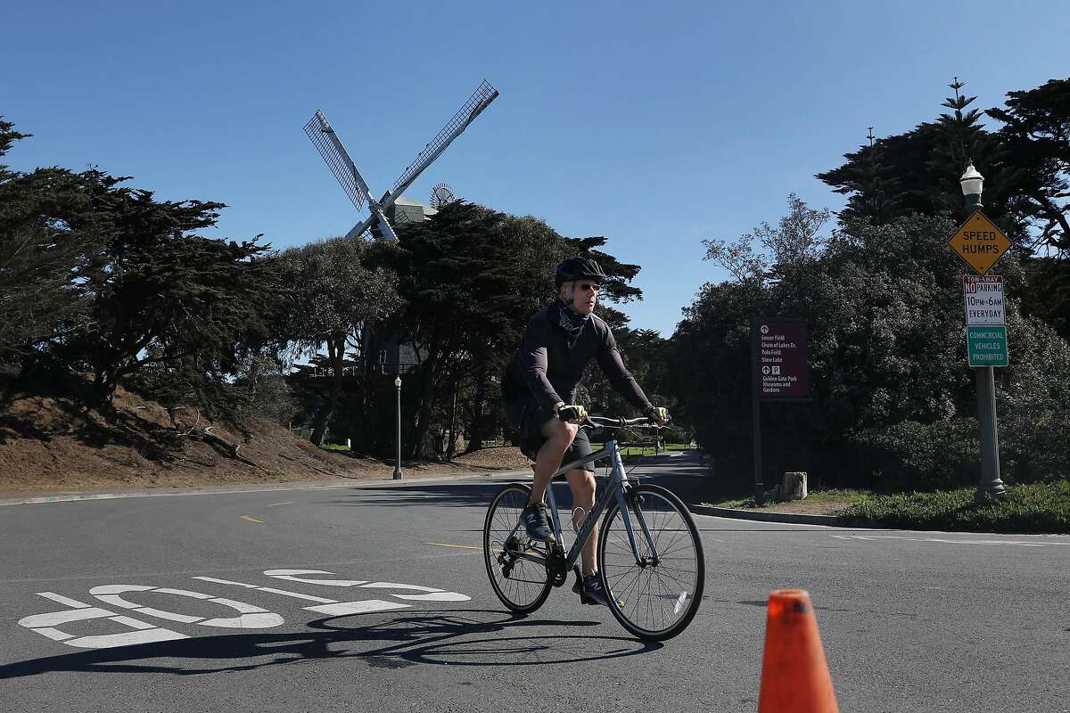 Bicyclists ride along on a “slow street” on MLK Drive past the Murphy Windmill in Golden Gate Park.