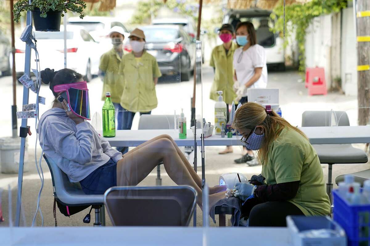 FILE - In this July 22, 2020, file photo, Tyson Salomon, left, gets a pedicure outside Pampered Hands nail salon in Los Angeles. Dr. Mark Ghaly, the state health secretary, said nail salons could also reopen with restrictions. The livelihoods of tens of thousands of mostly minority women hang in the balance as the coronavirus pandemic continues to affect the nail industry. (AP Photo/Ashley Landis, File)
