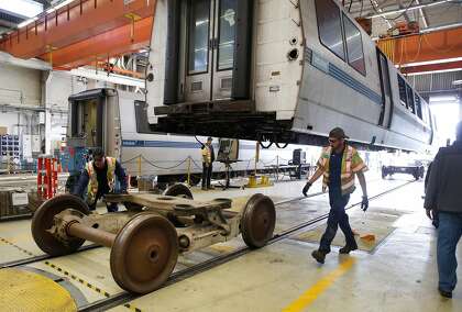 Maintenance workers roll temporary wheels away from a retired BART car before it is lowered onto a flatbed truck at the BART maintenance yard in Hayward, Calif. for transfer to a scrapyard on Friday, Nov. 8, 2019. Placed into service in 1995 and after logging more than 2.2 million miles, car number 2528 is the first of the transit agency's fleet of the past to be scrapped now that 58 of the "fleet of the future" cars are in service.