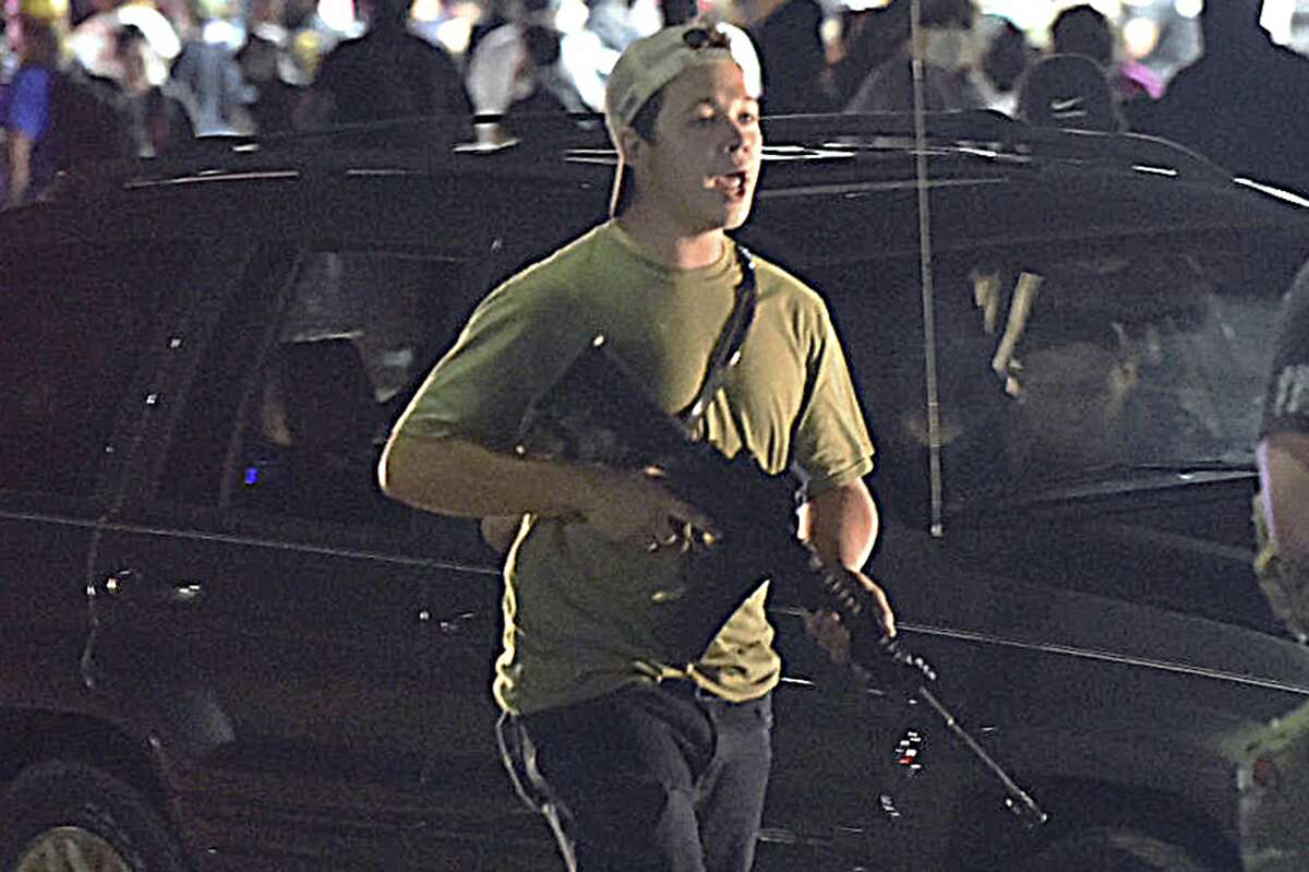 In this Tuesday, Aug. 25, 2020 file photo, Kyle Rittenhouse carries a weapon as he walks along Sheridan Road in Kenosha, Wis., 
