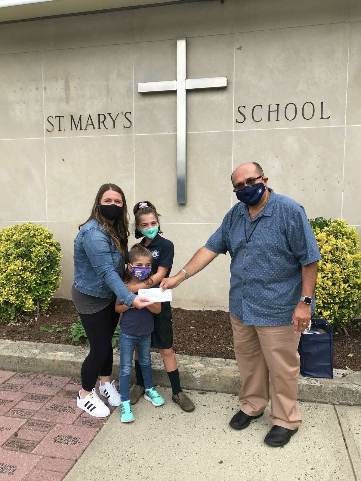 Danielle Hogan and her daughters Brooklyn and Devyn present a check for $1,000 from the St. Mary's pizza night fundraiser to Principal Deacon Dominic Corraro.