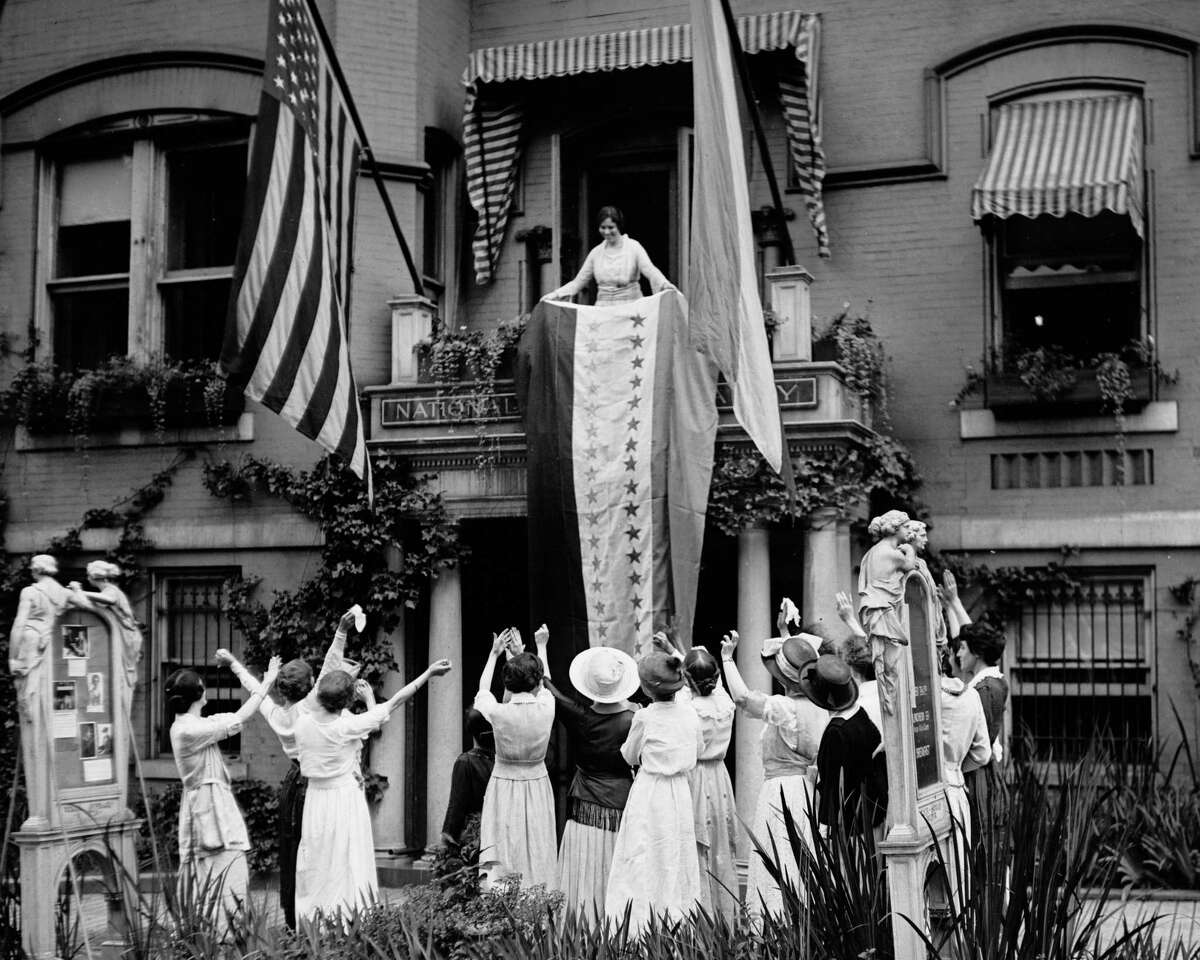 In this Aug. 19, 1920 photo made available by the Library of Congress, Alice Paul, chair of the National Woman's Party, unfurls a banner after the ratification of the 19th Amendment, at the NWP's headquarters in Washington.