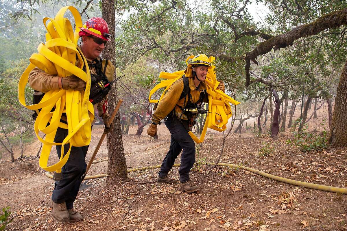 San Diego County firefighters Mike Terlouw and Robert Scott carry fire hose up to a spot fire behind Schramsberg Winery during the Glass Fire in Calistoga on Tuesday.