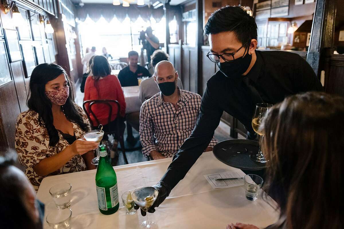 Server Nat Chananudech wears a mask and gloves as he delivers drinks to guests at John's Grill in San Francisco in September.