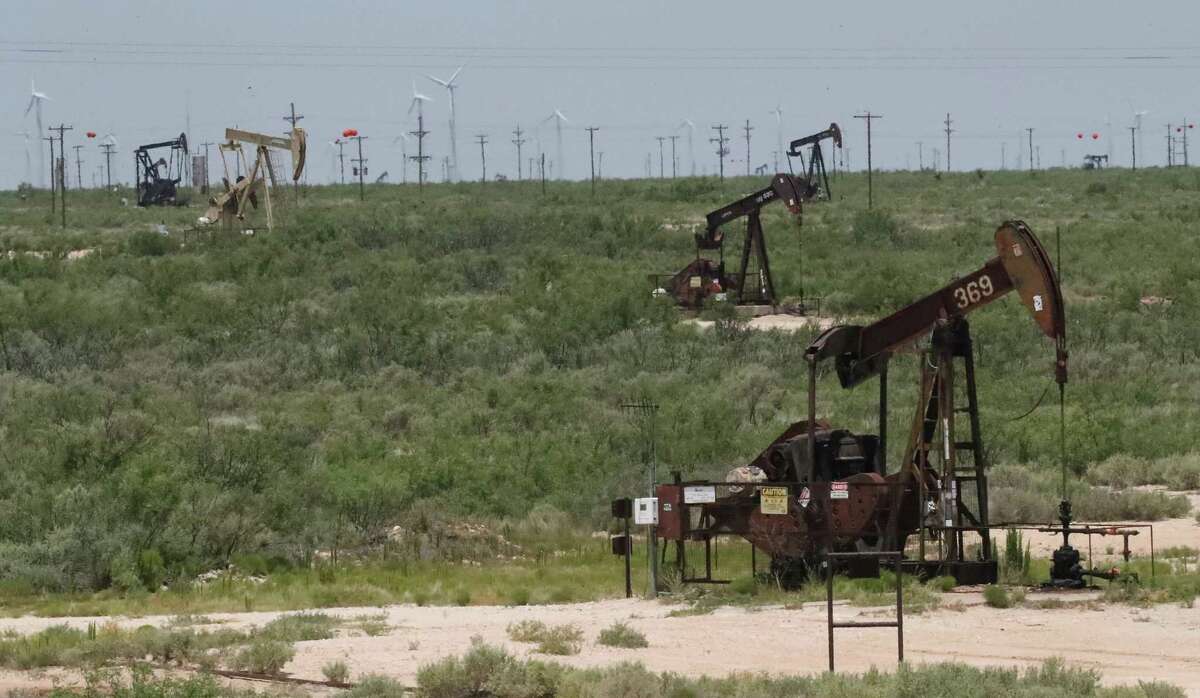 Pump jacks are stacked in front of rows of a windmill field in West Texas Wednesday, June 28, 2017 outside of Kermit, Texas. ( Steve Gonzales / Houston Chronicle )