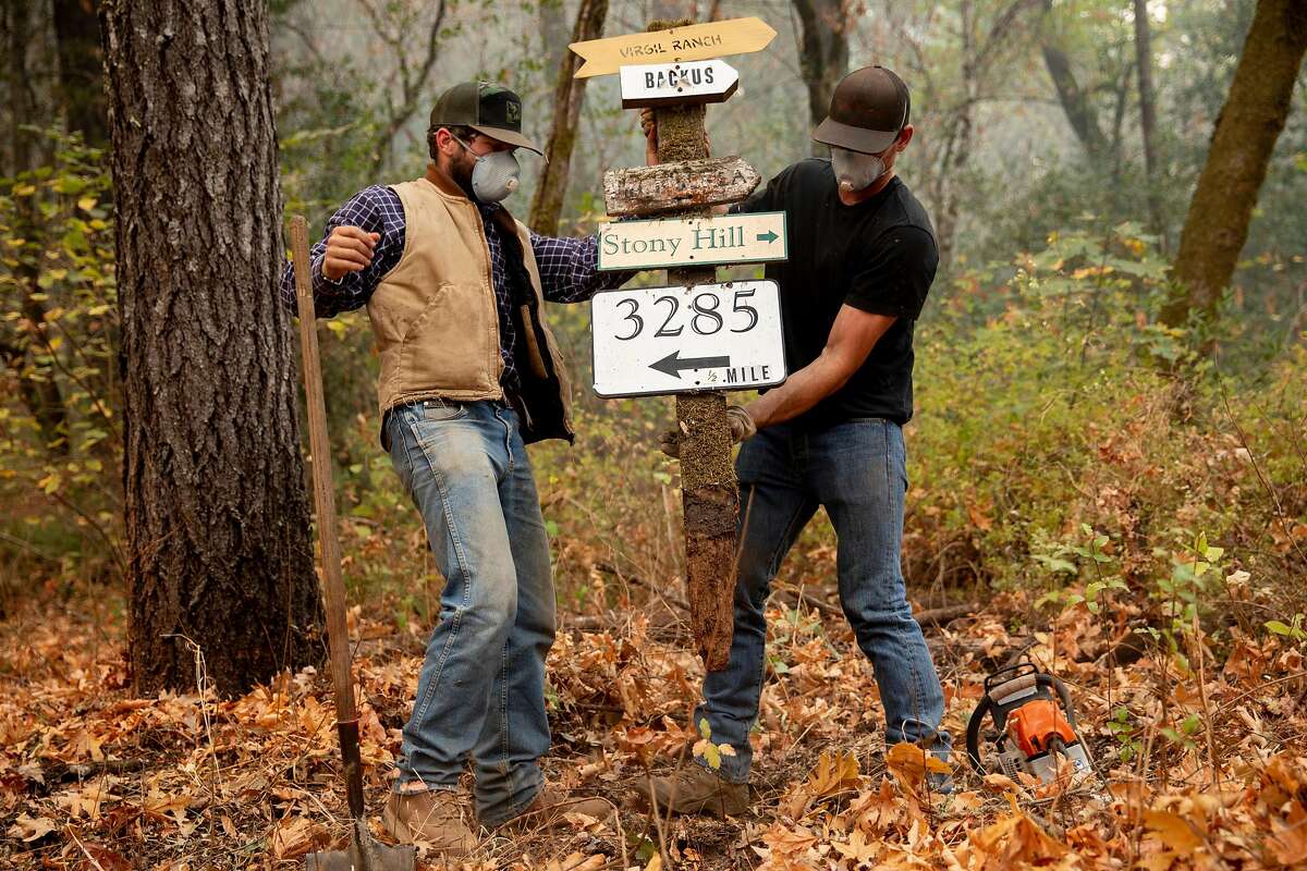 Russell Tobiass (left) and Matteo Abreu of David Abreu Vineyard Management work to remove a road sign and clear brush to allow water trucks to access Stony Hill Vineyard as the Glass Fire burns on its property in St. Helena, Calif. Thursday, October 1, 2020. Fire crews from Contra Costa County, Moraga-Orinda and Rodeo-Hercules fire departments worked through Wednesday day and night to protect structures at Stony Hill Vineyard and were successful, although the surrounding property suffered fire damage. The Glass Fire has burned more than 56,000 acres in Napa and Sonoma counties by Thursday morning and is 5% contained.
