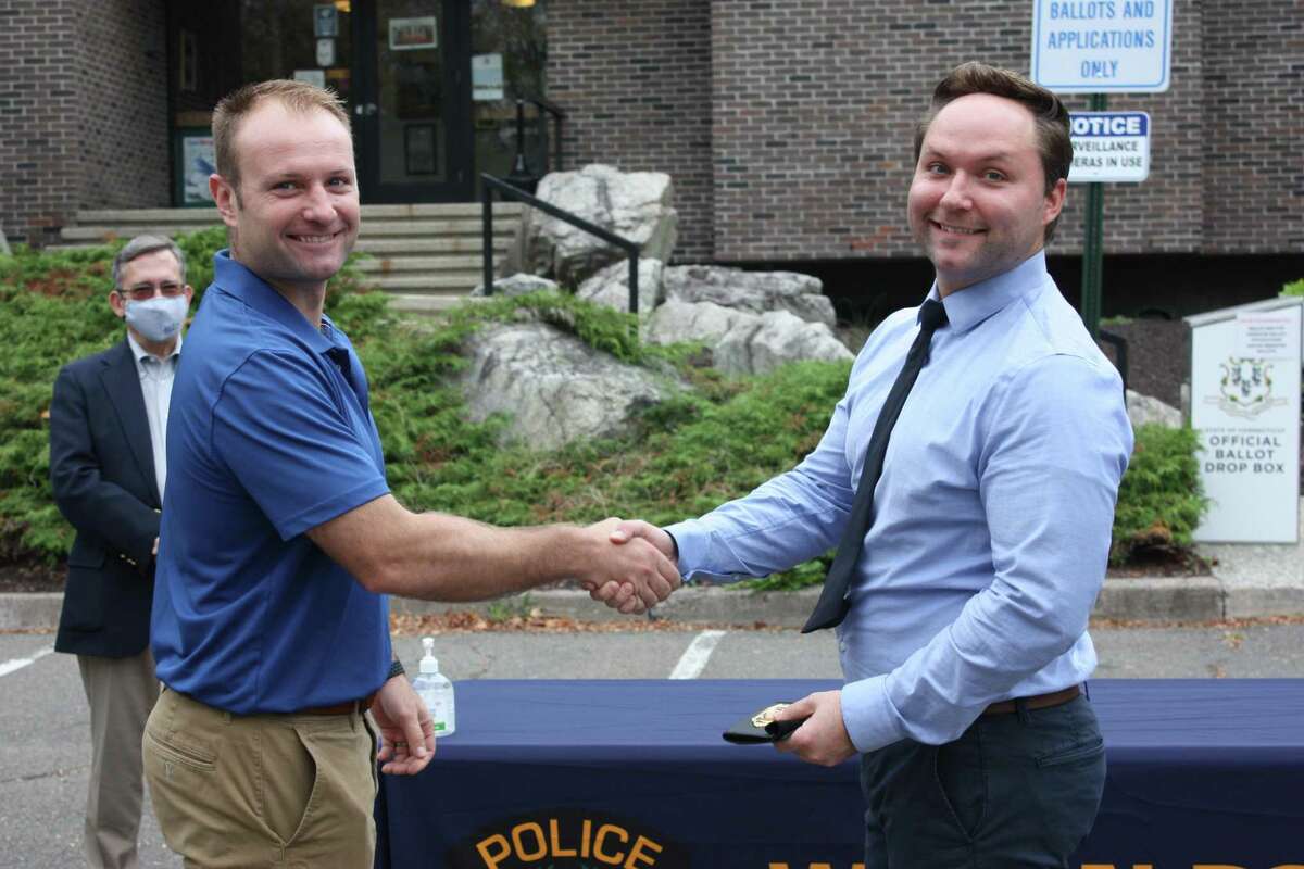 Newly promoted Detective Edward Dolenk, right, receives his badge from his brother, Max Dolenk, who is an officer with the New York City Police Department, during a ceremony at Wilton Police Headquarters on Sept. 29. In the background is Police Commissioner David Waters.