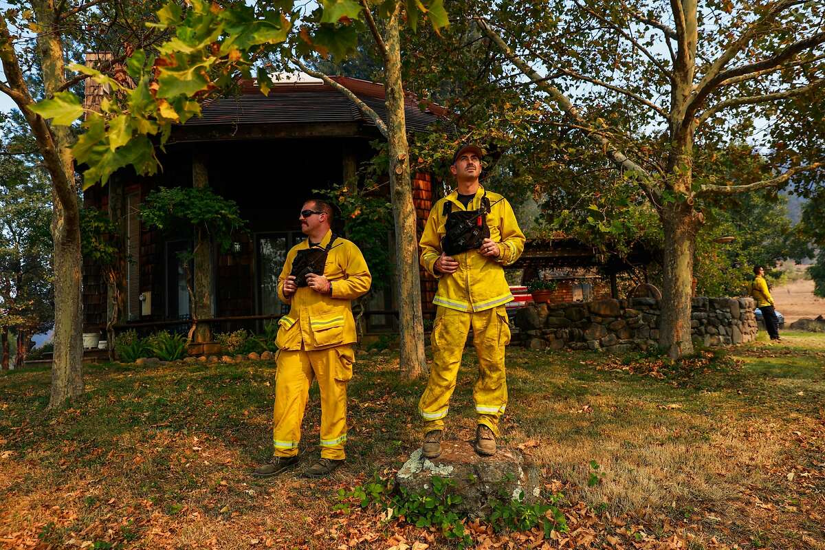 (L-r) Firefighters Dave Novelli and Scott Sousa watch a helicopter drop over the Glass Fire off of Highway 29 as they keep watch over a threatened house on Sunday, Oct. 4, 2020 in Calistoga, California.