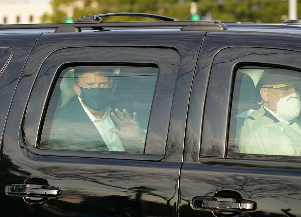 President Trump waves from the back of a car in a motorcade outside of Walter Reed Medical Center on Sunday. The trip has drawn criticism due to the risk to others in the car.