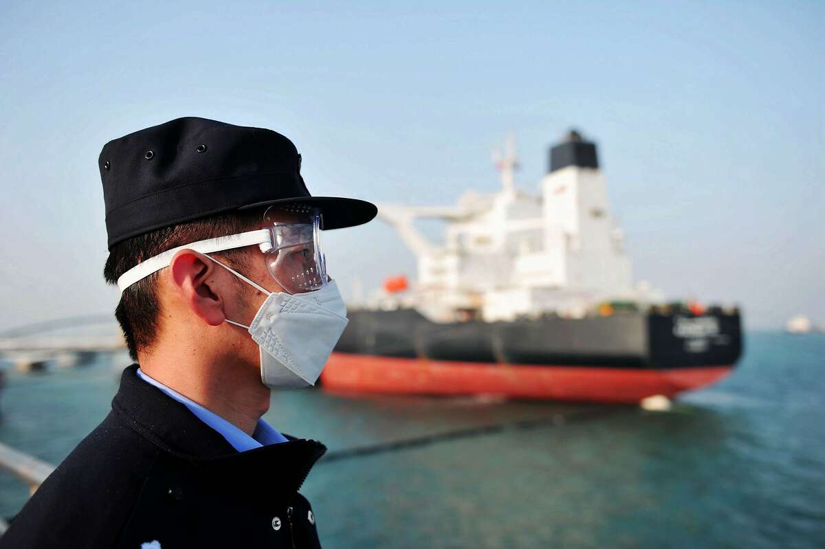 This photo taken on March 20, 2020 shows a police officer wearing a mask amid concerns over the COVID-19 coronavirus while keeping watch as a Kuwaiti oil tanker unloads crude oil at the port in Qingdao, in China's eastern Shandong province. (Photo by STR / AFP) / China OUT (Photo by STR/AFP via Getty Images)