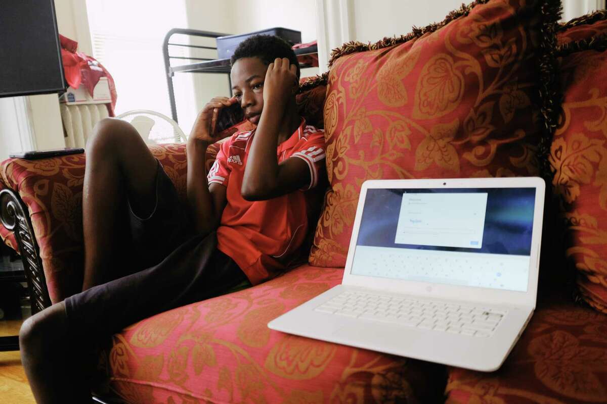Paul Buckowski's images of a refugee family grappling with the challenges of distance learning were honored by the state News Publishers Association. Above: Mlondani Mnyomoelwa, a seventh grader in the Albany School district, waits on hold for help on resetting his password to be able to sign in to his Chromebook.